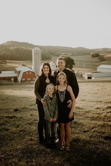 A family is posing for a picture in a field with a barn in the background. A family is posing for a picture in a field with a barn in the background.
