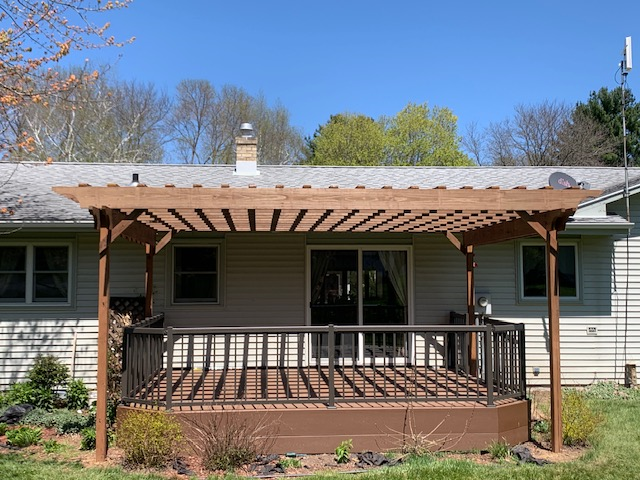 A wooden deck with a pergola extends from a house with a sliding glass door.
