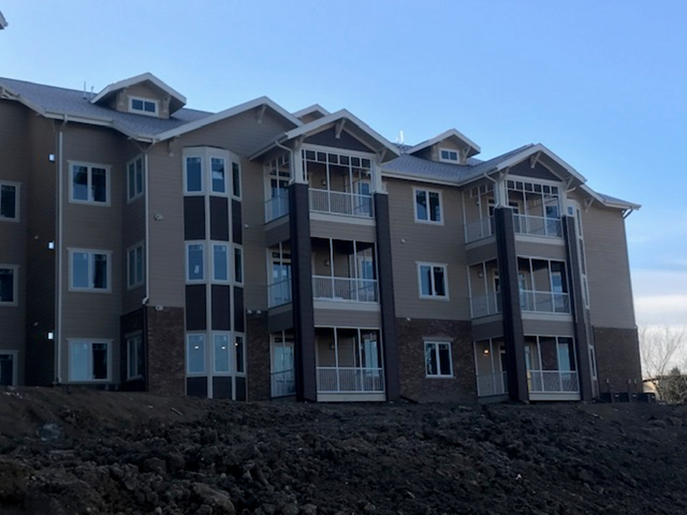 Multi-story apartment building under construction, exterior view. Tan and brown siding, balconies, against a blue sky.