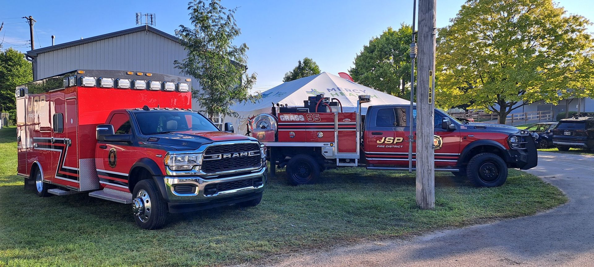 Two red fire trucks and an ambulance parked near a building and a tent.