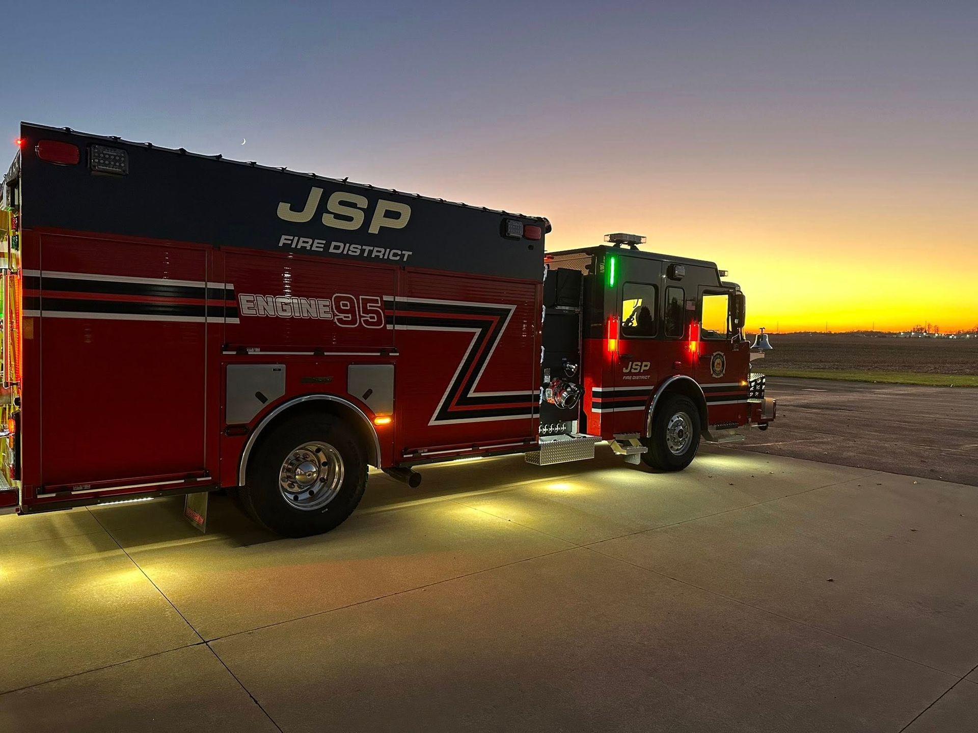 Red and black JSP fire truck with lights on at dusk.