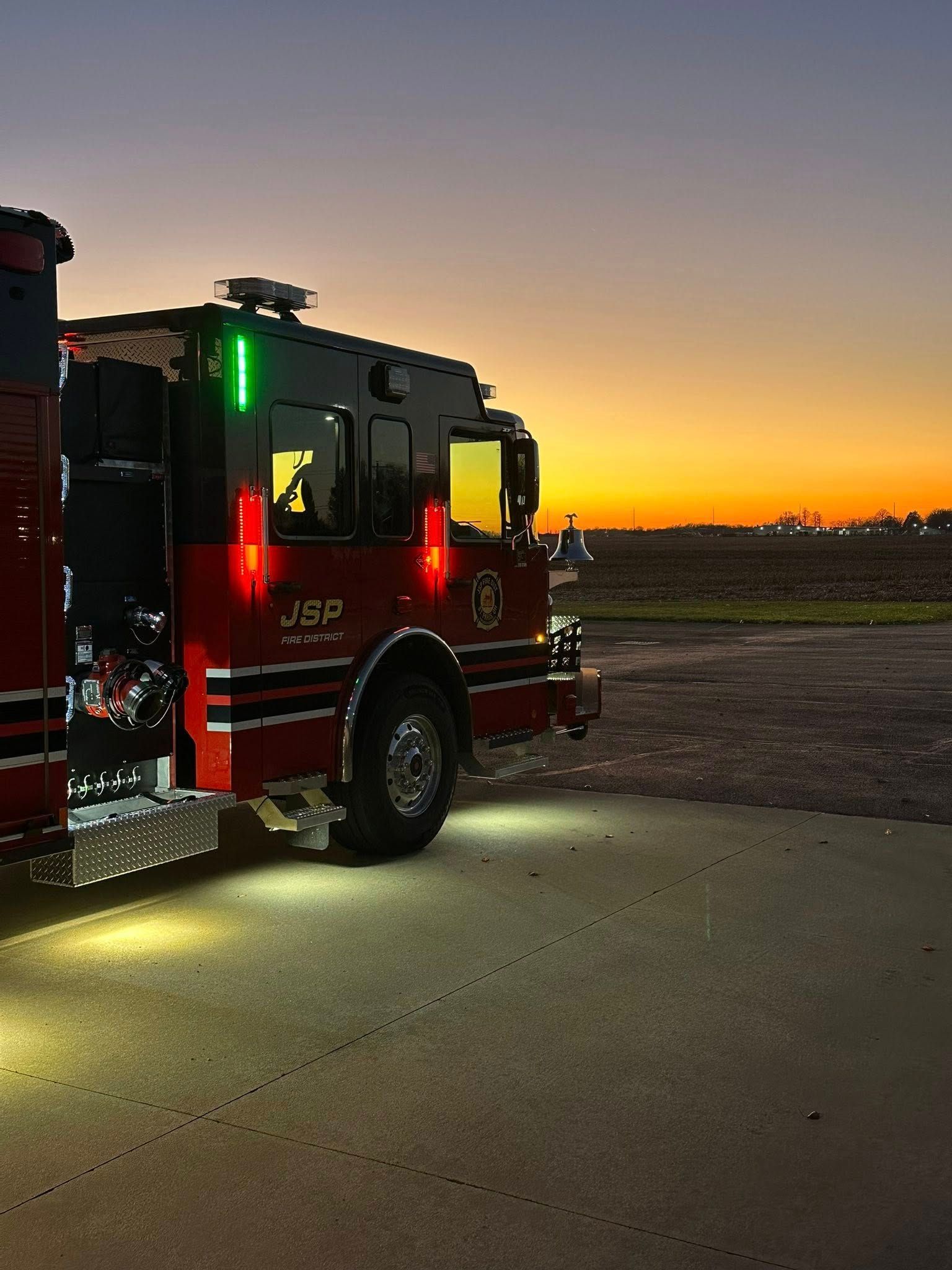 Fire truck parked on asphalt at sunset; red and black with emergency lights.