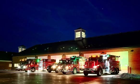 Fire trucks parked at a station at night, illuminated by green and red lights.