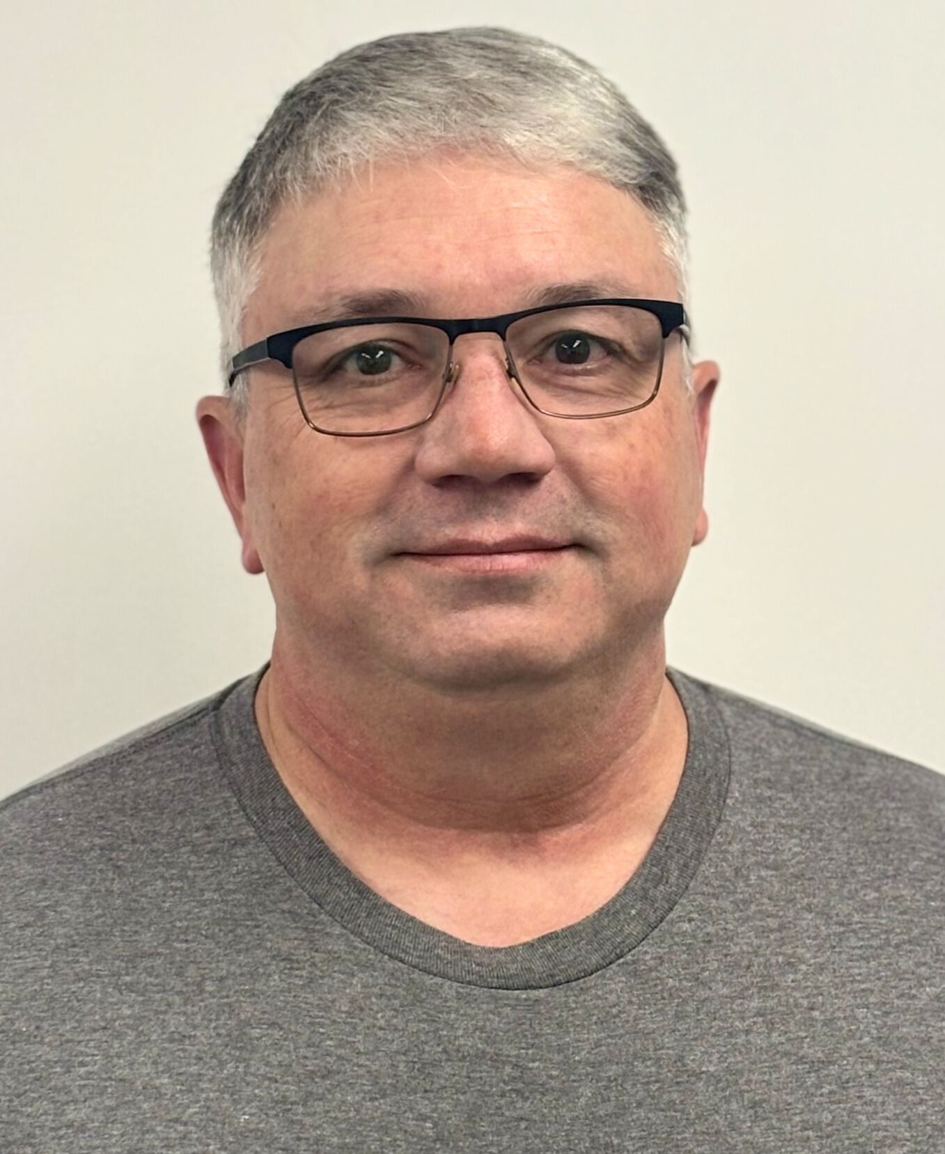 Man wearing glasses, gray t-shirt, looking at the camera against a white background.