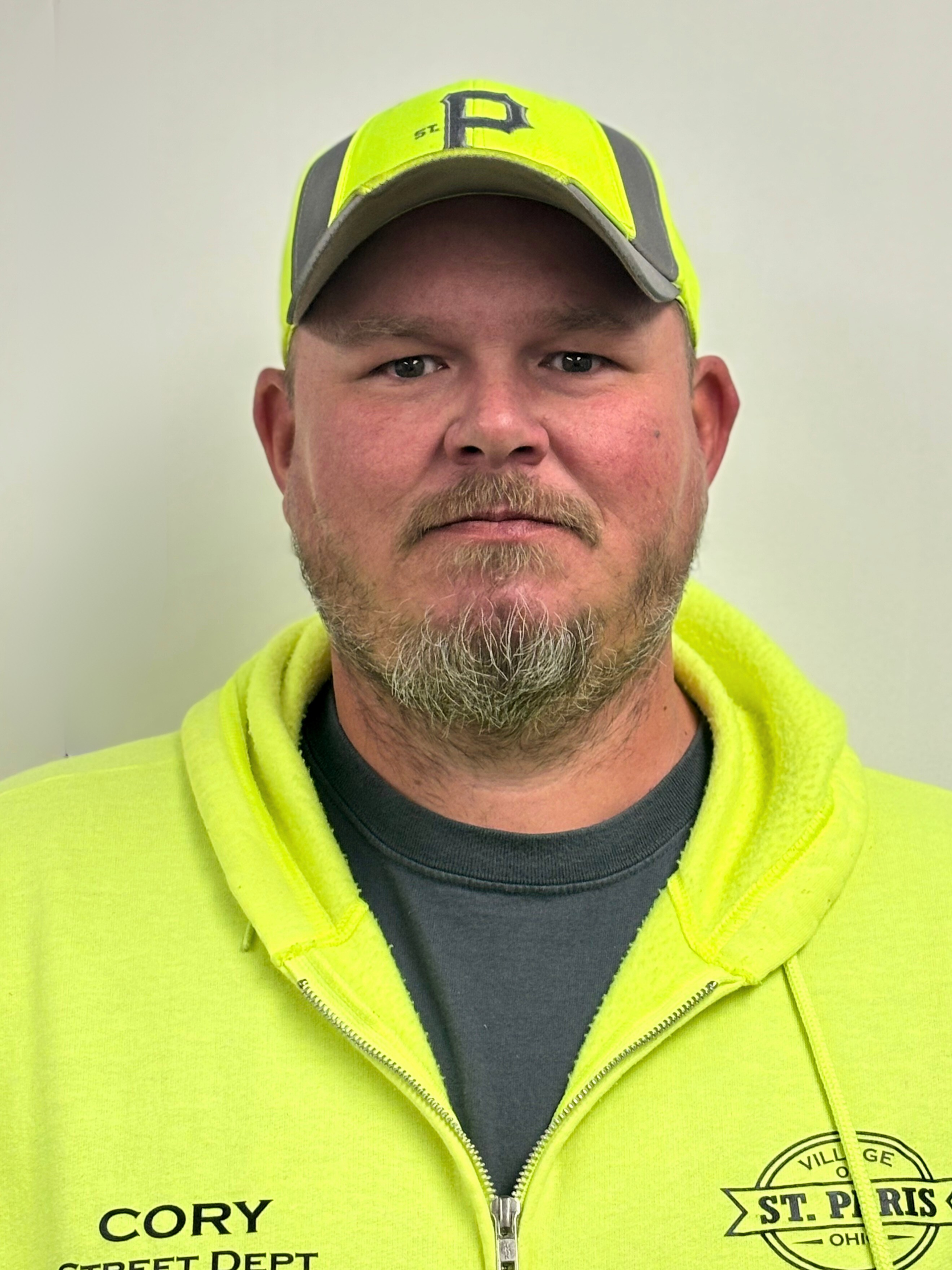 Man wearing neon yellow safety gear, including a hat and jacket, in front of a white wall.