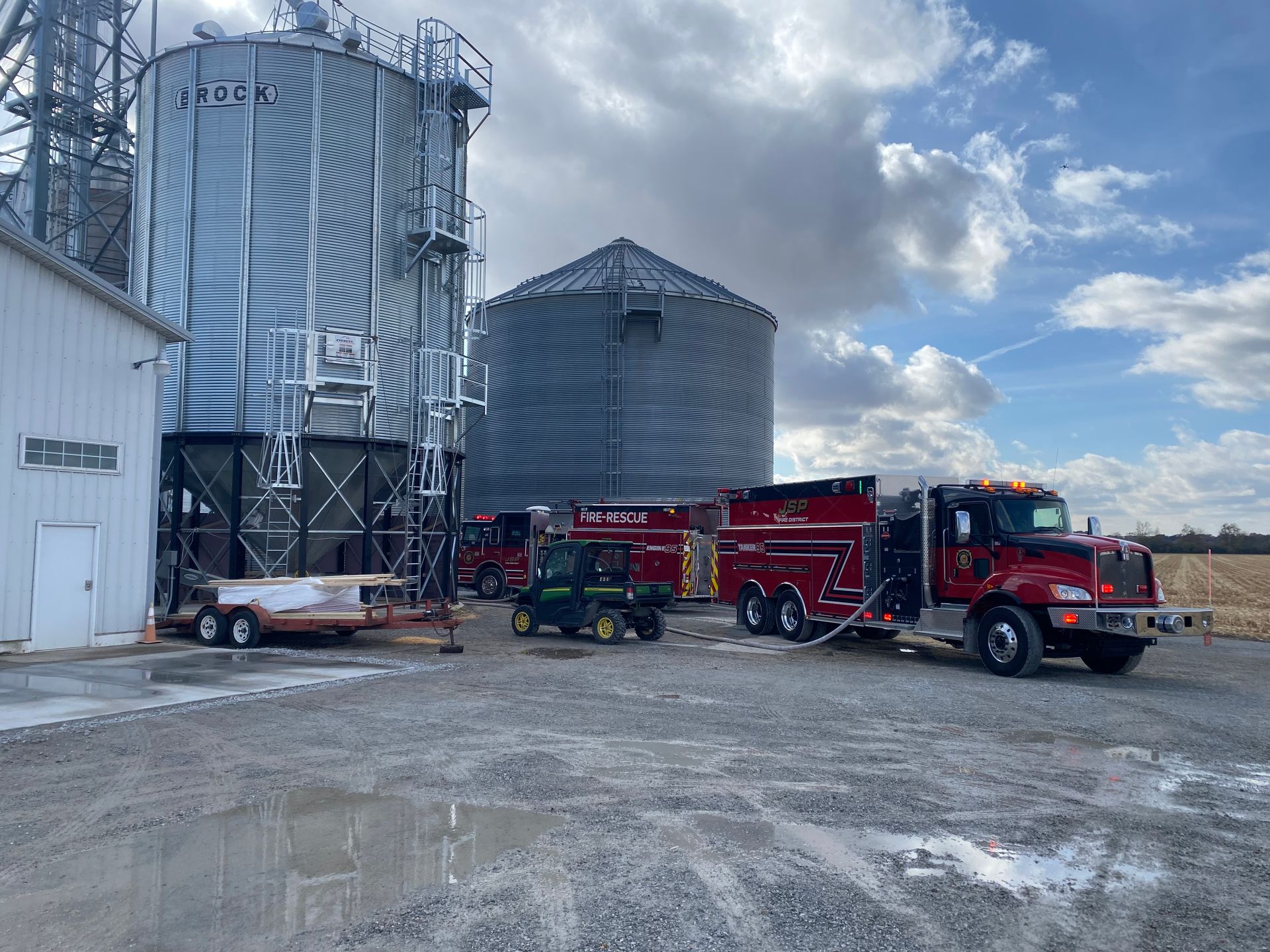 Fire trucks and equipment at a grain silo, likely responding to an incident. Cloudy sky.