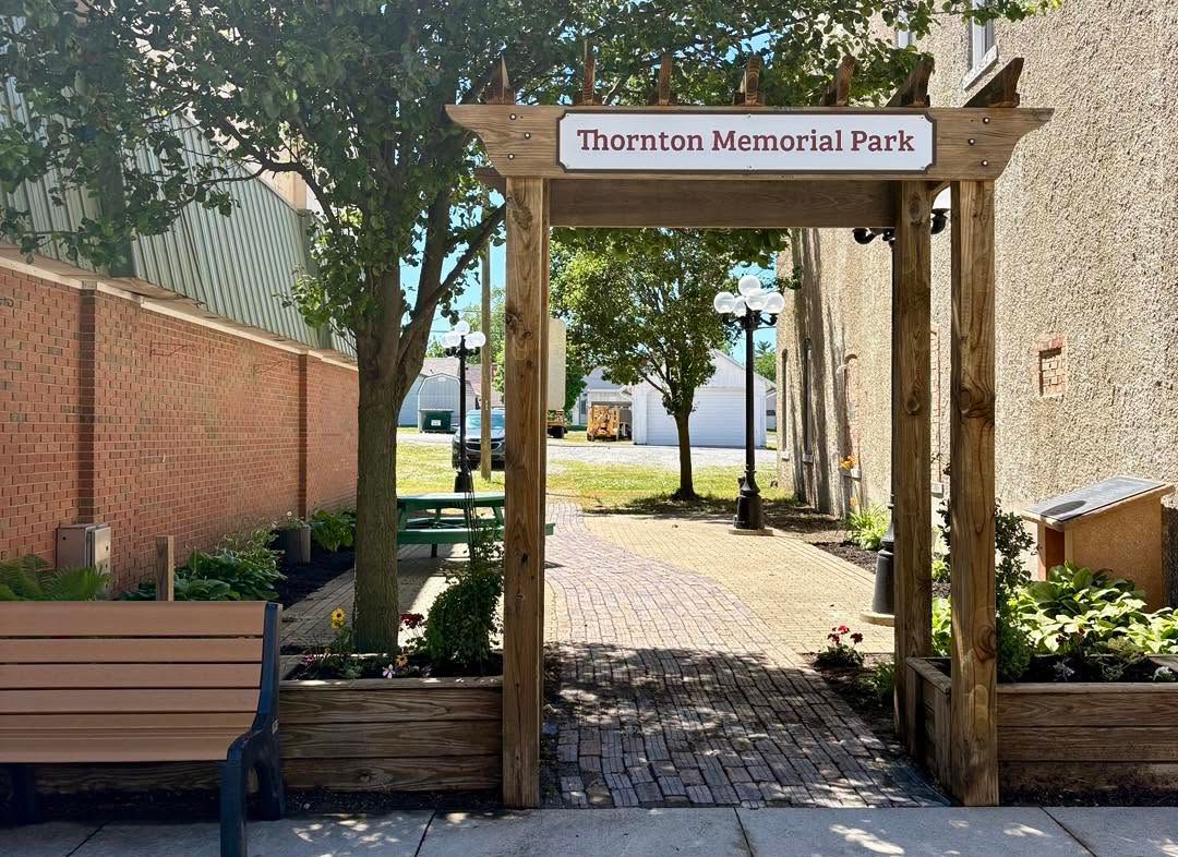 Wooden entrance arch to Thornton Memorial Park along a cobblestone path with benches and flowers