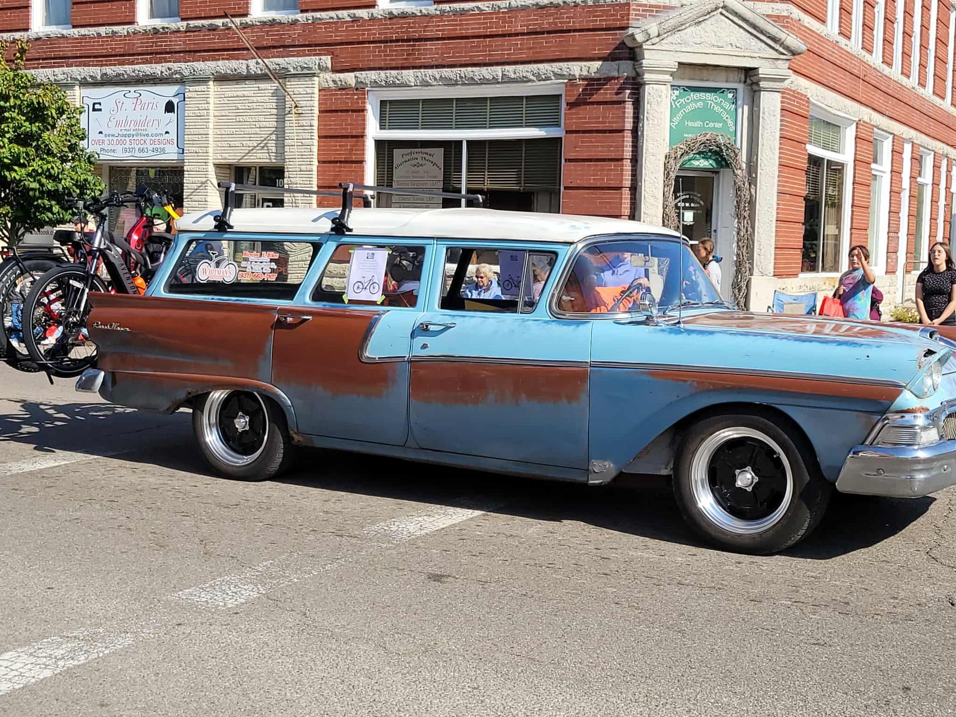 Blue and rust-colored vintage station wagon parked on a street in front of a brick building.
