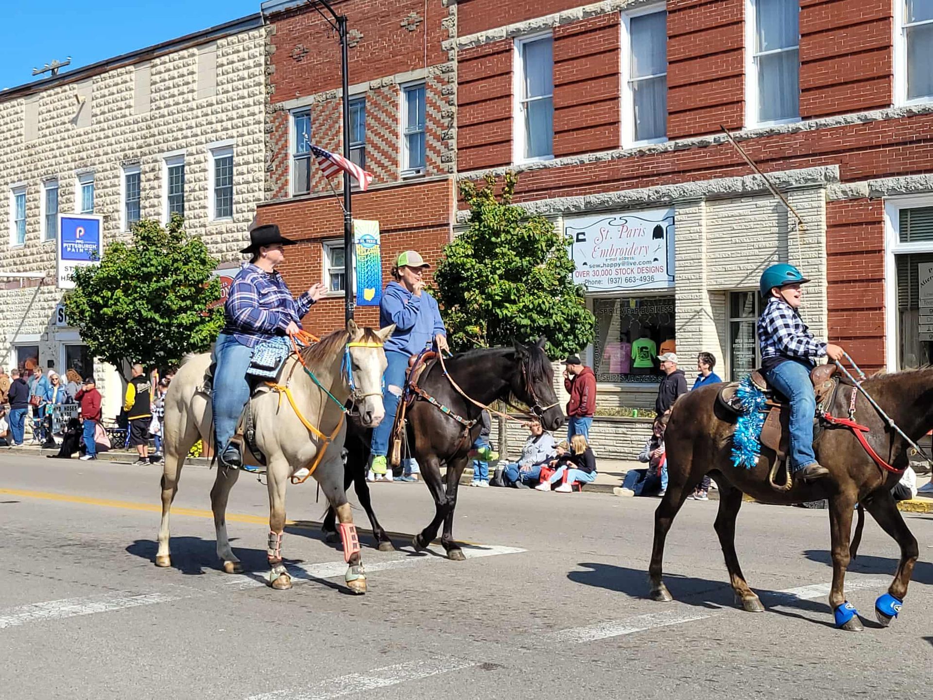 Three people riding horses in a parade; brick buildings in background.
