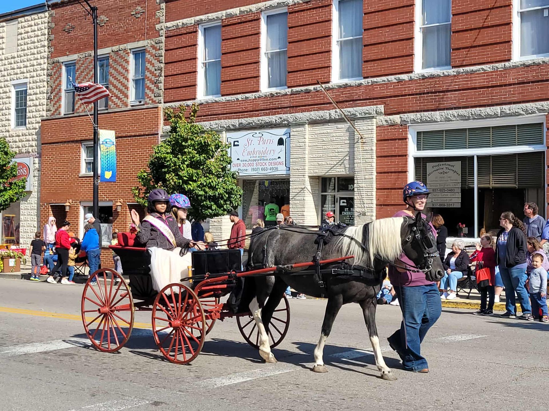Horse-drawn carriage in a street parade, people watching along brick buildings.