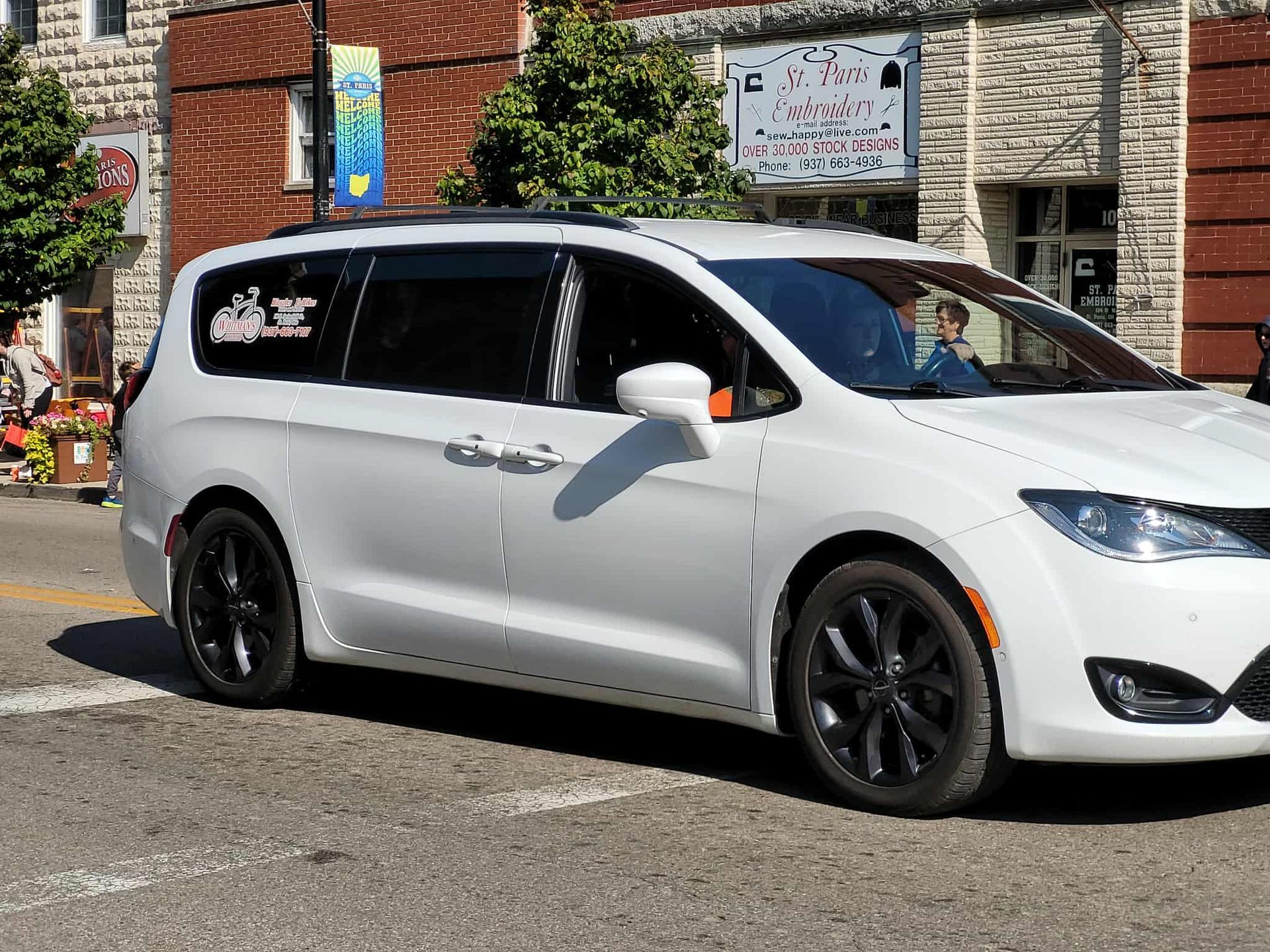 White minivan with black wheels on a city street.