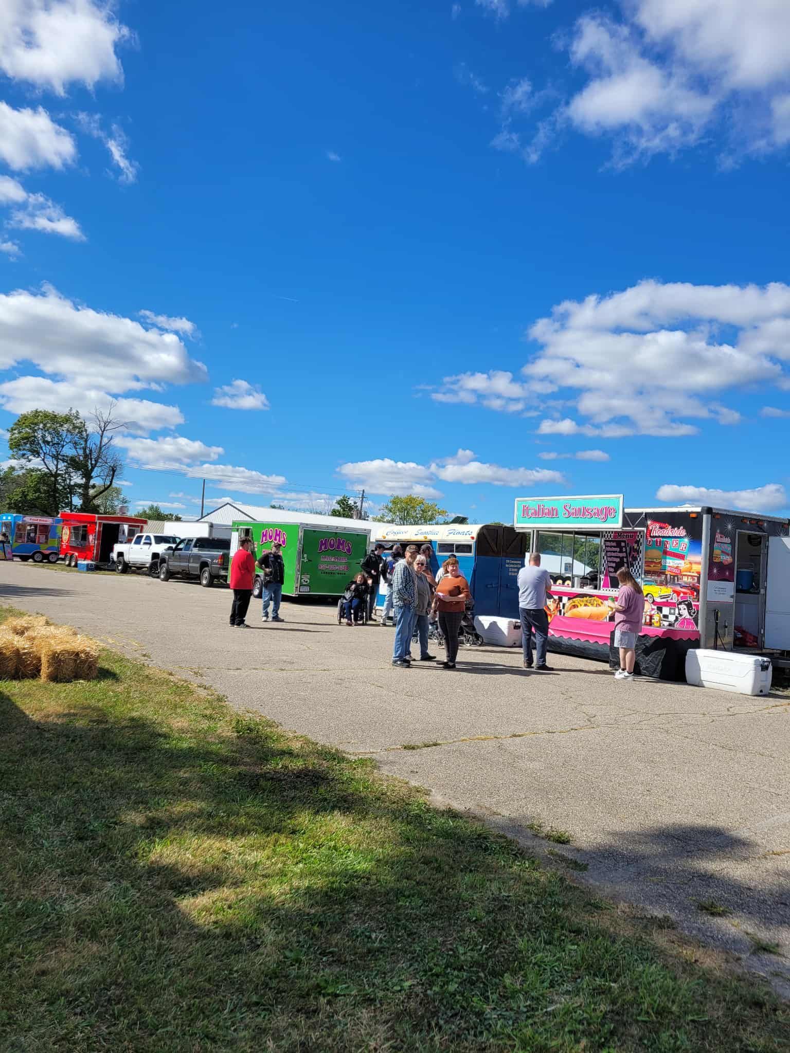 Food vendors and people at outdoor fair on a sunny day.
