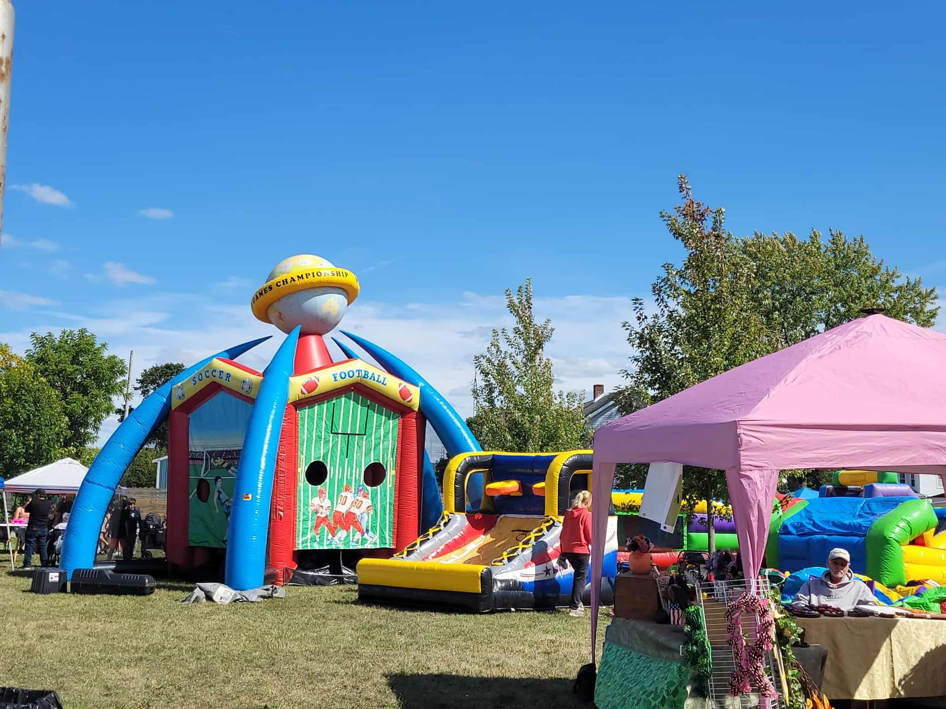 Inflatable play structure at outdoor event with tents and people on a sunny day.
