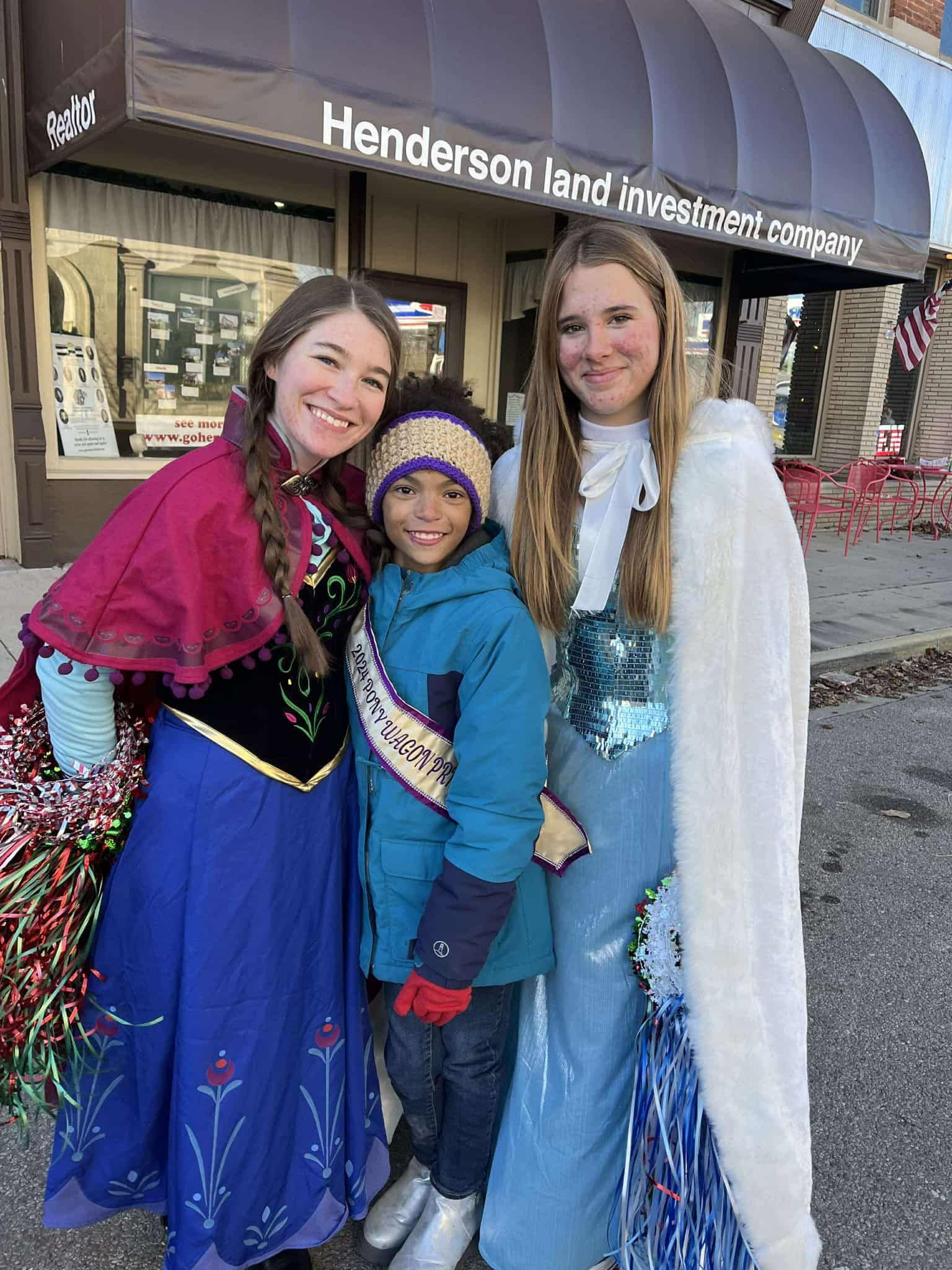 Three people dressed as Frozen characters pose outside a building.
