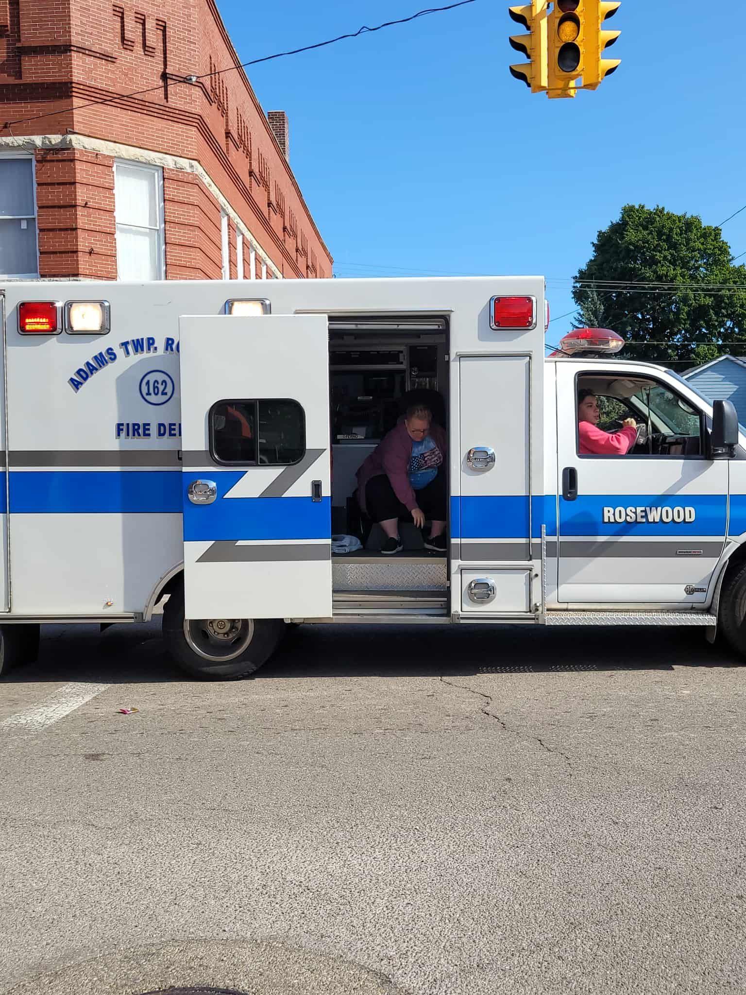 Ambulance with open door; two people inside, one child; brick building background.