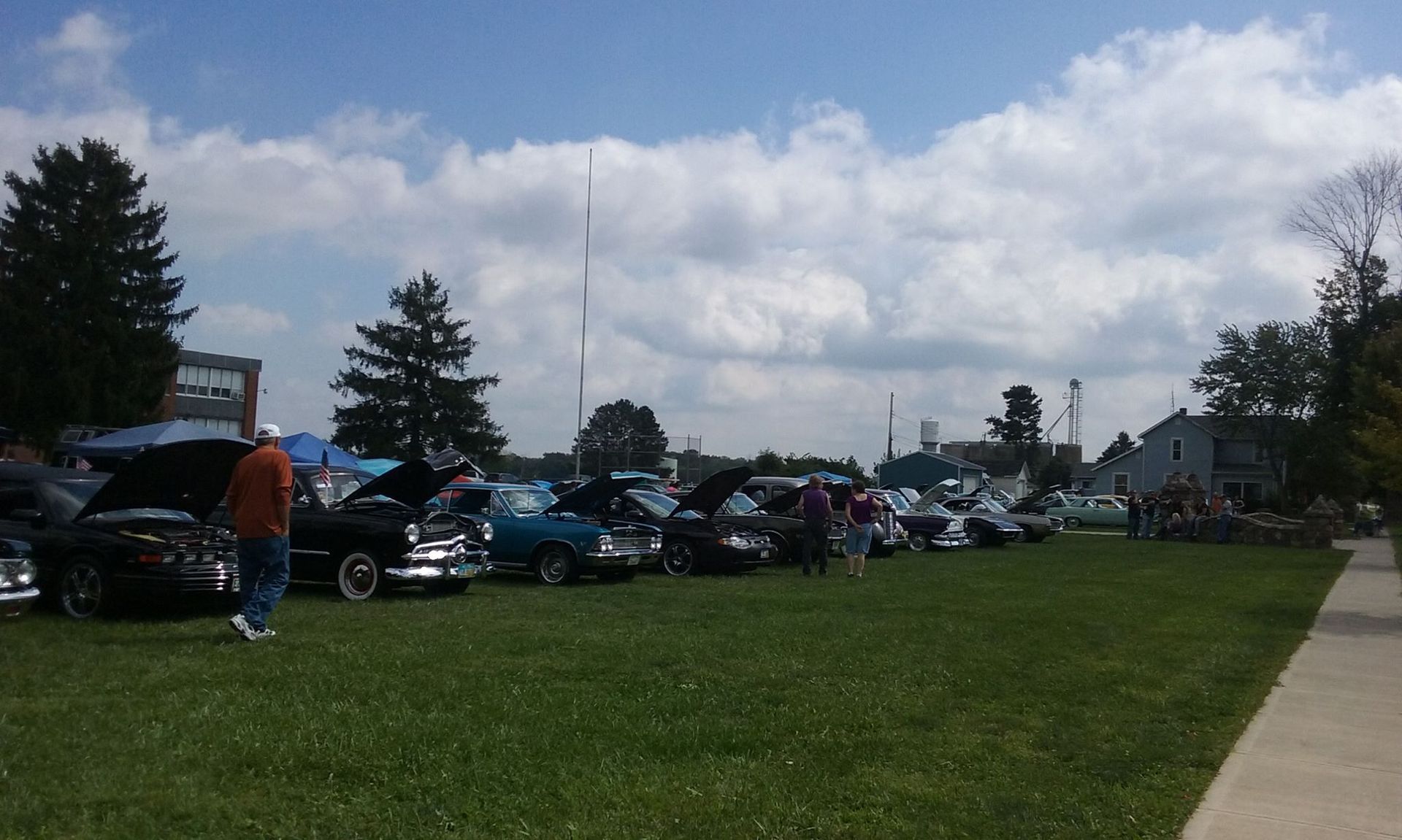 Classic cars on display at an outdoor event on a grassy field under a partly cloudy sky.