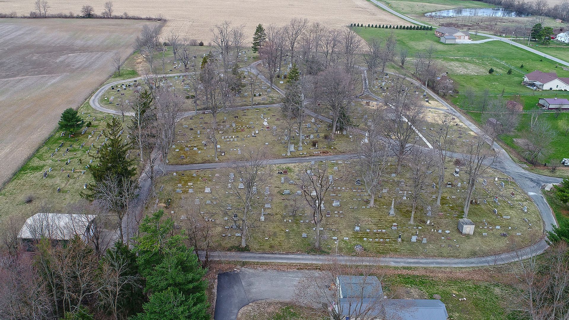 Aerial view of a cemetery with numerous headstones among trees and winding pathways.