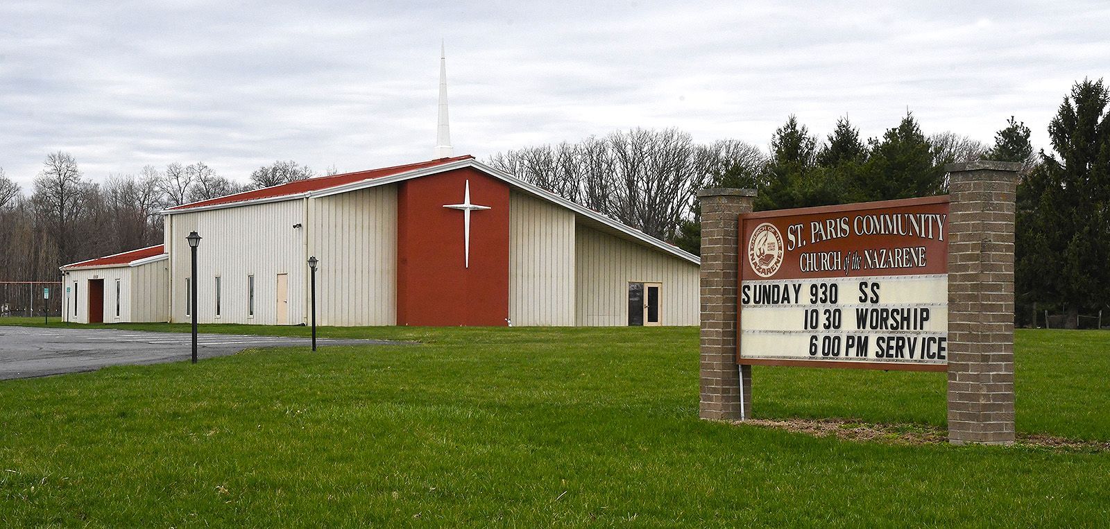 Church building with red accents, a cross, and a sign on a green lawn.