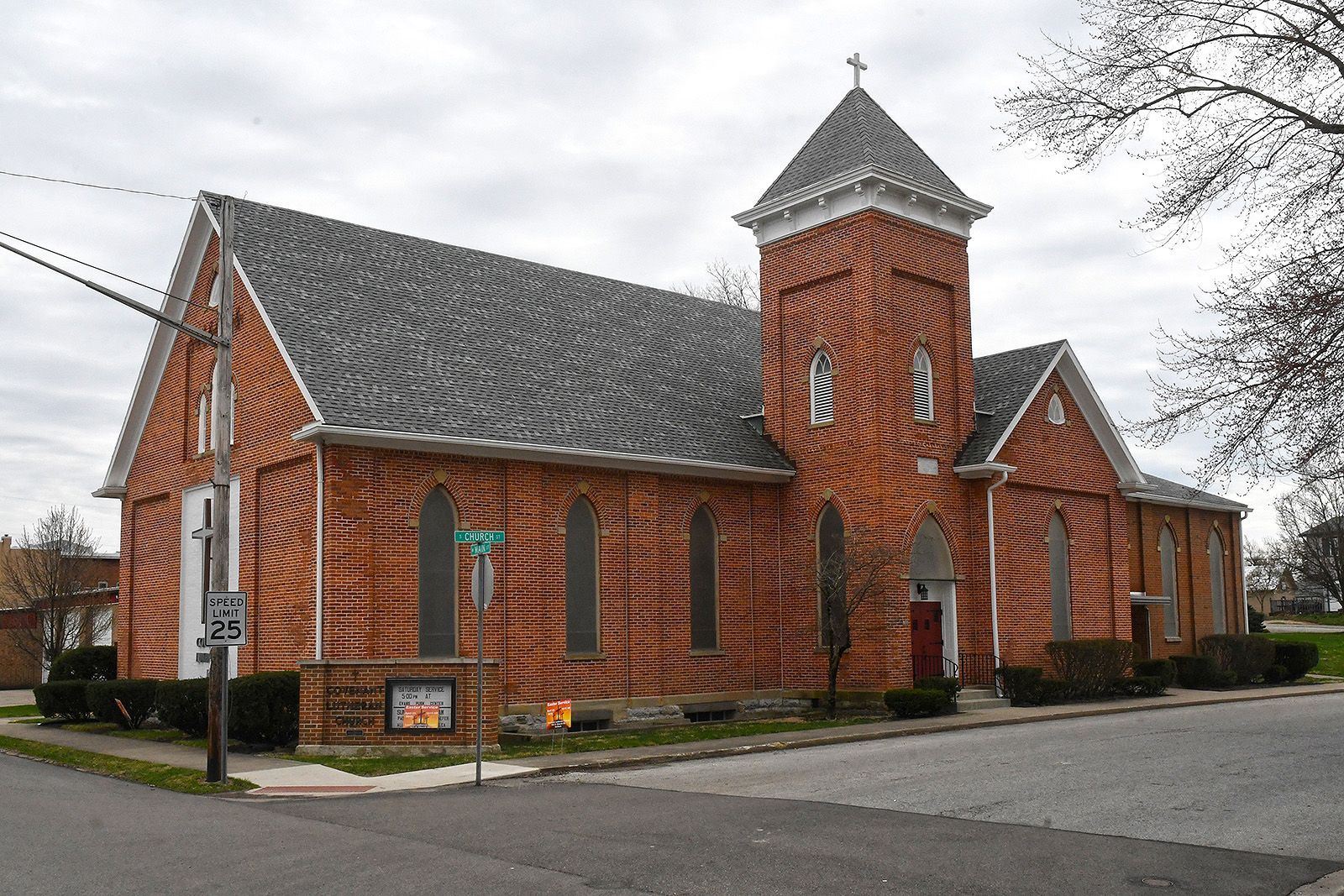 Brick church building at a street corner with a gray roof and a steeple.