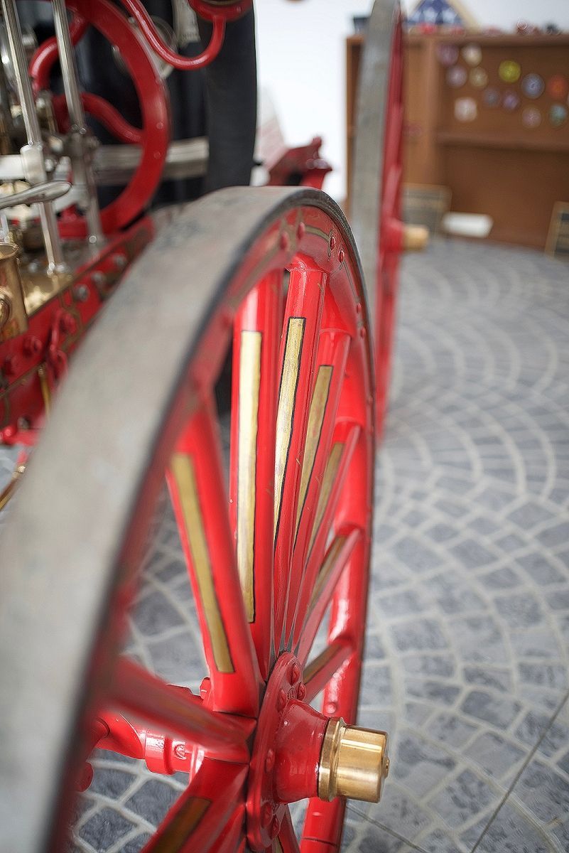 Close-up of a red and gold spoked wheel on a vehicle. The tire is gray, and the setting appears to be indoors.