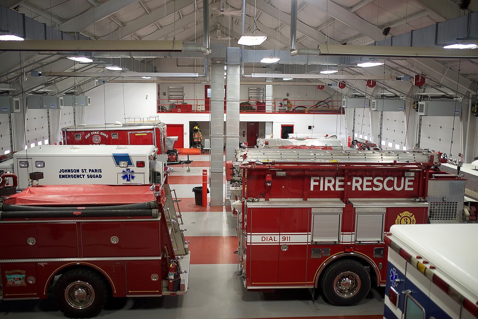 Inside a fire station: red fire trucks and emergency vehicles are parked inside a large bay.