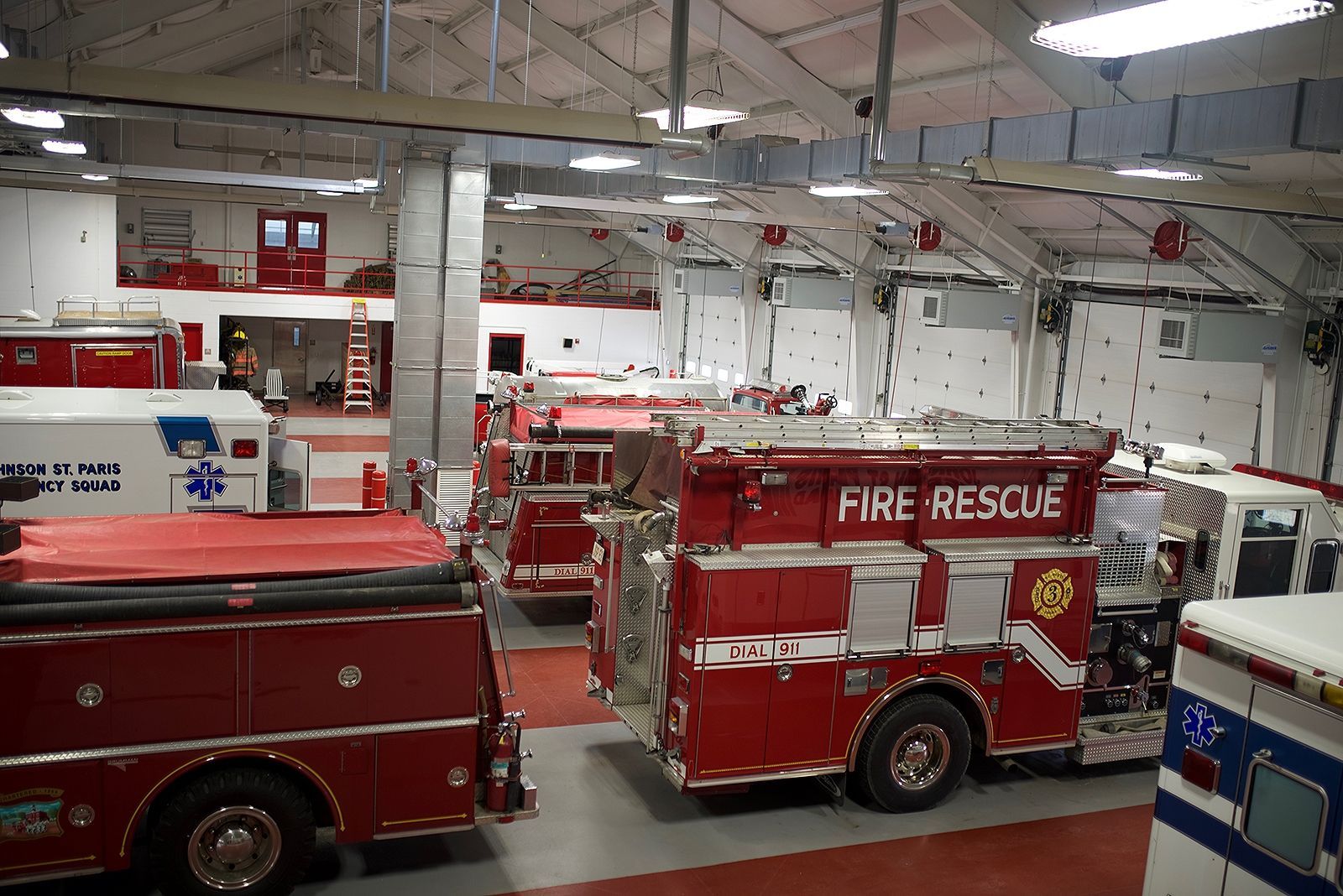 Fire station interior with red fire trucks and an ambulance parked inside the garage bays.