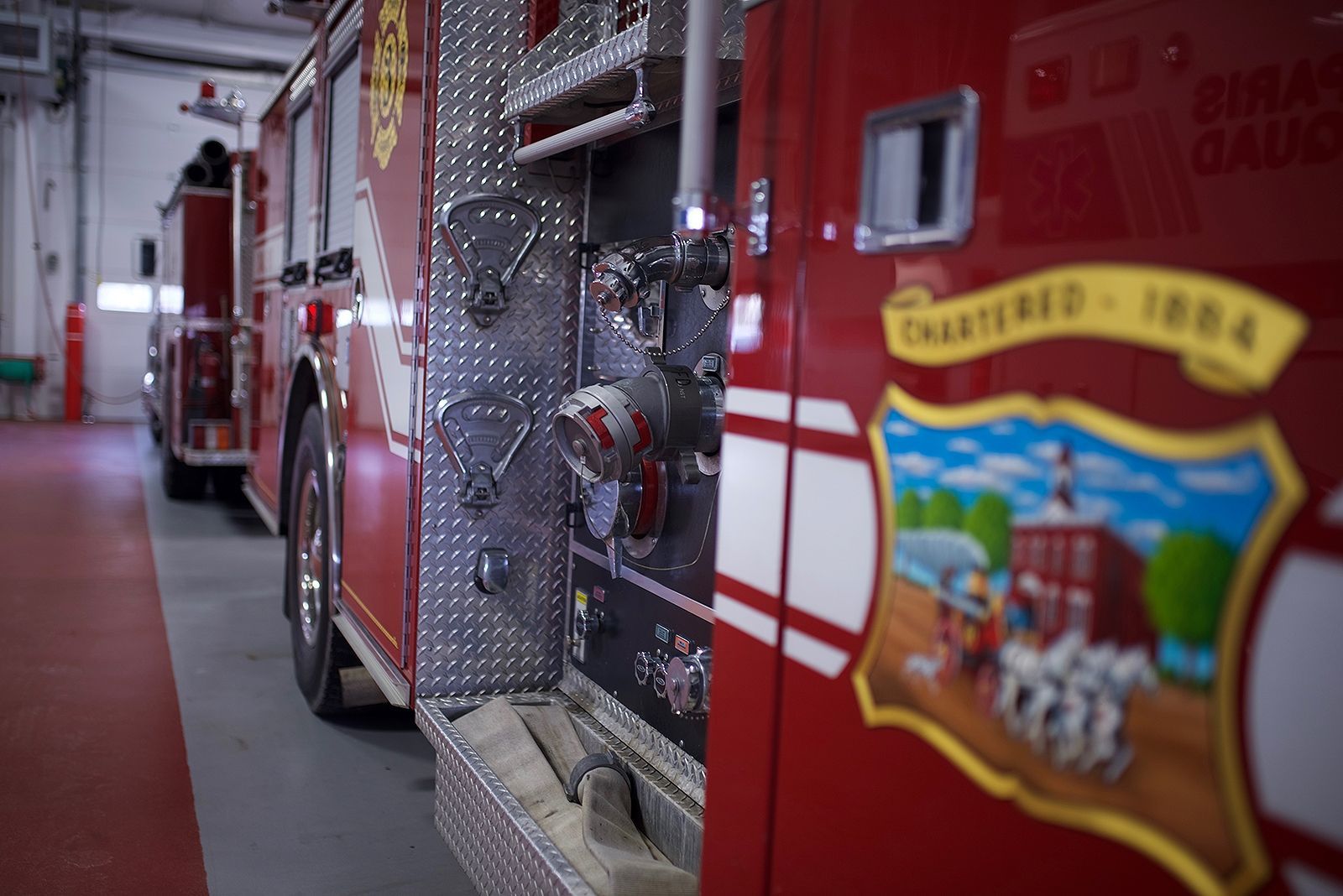 Red fire trucks parked inside a fire station, close-up of side with emblem.
