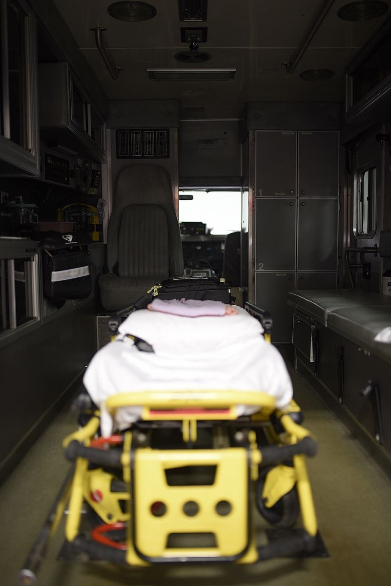 Interior view of an ambulance. A gurney with a white sheet is centered; storage compartments line the walls.