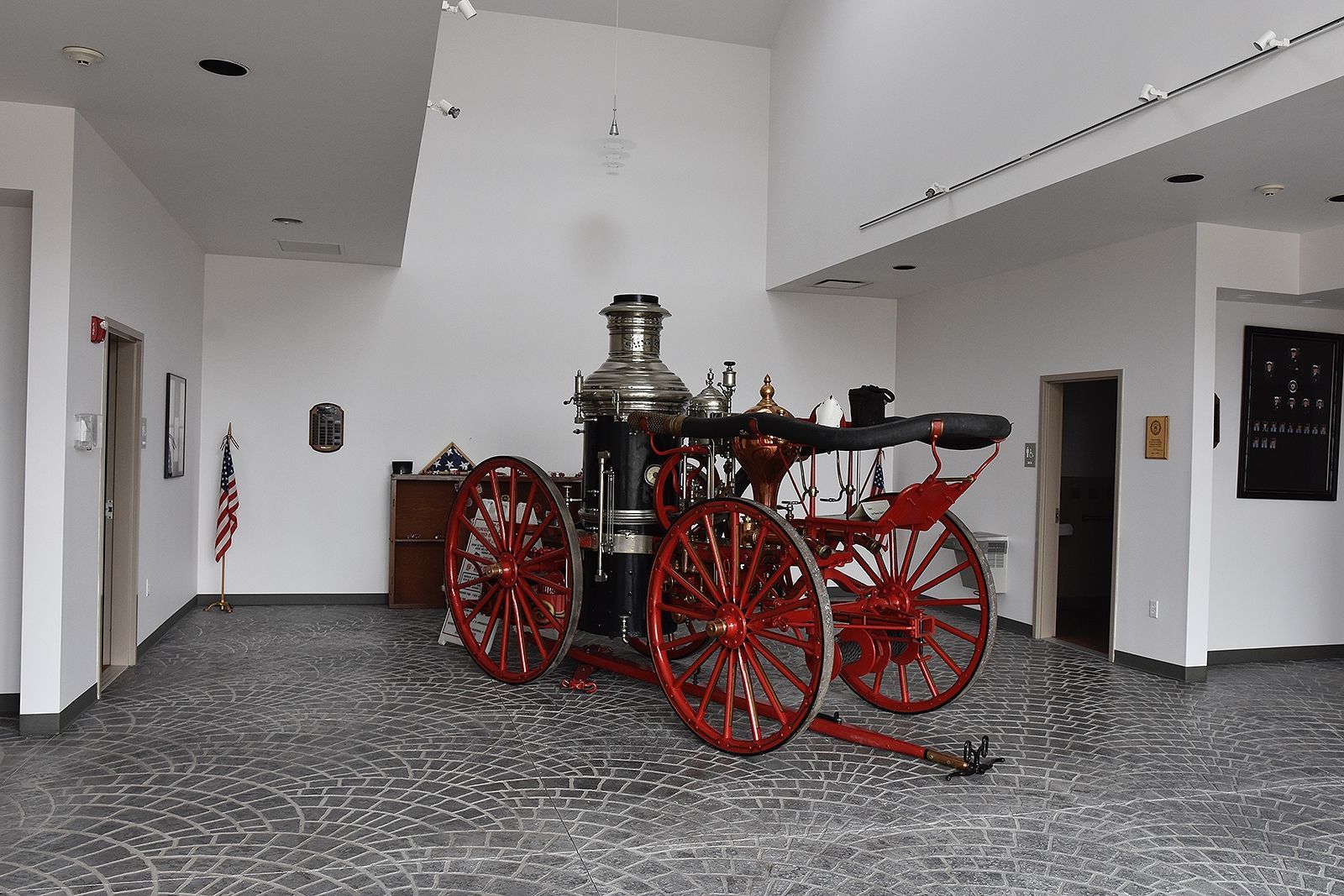 Antique red and black fire engine on display in a modern, well-lit museum gallery with an American flag.
