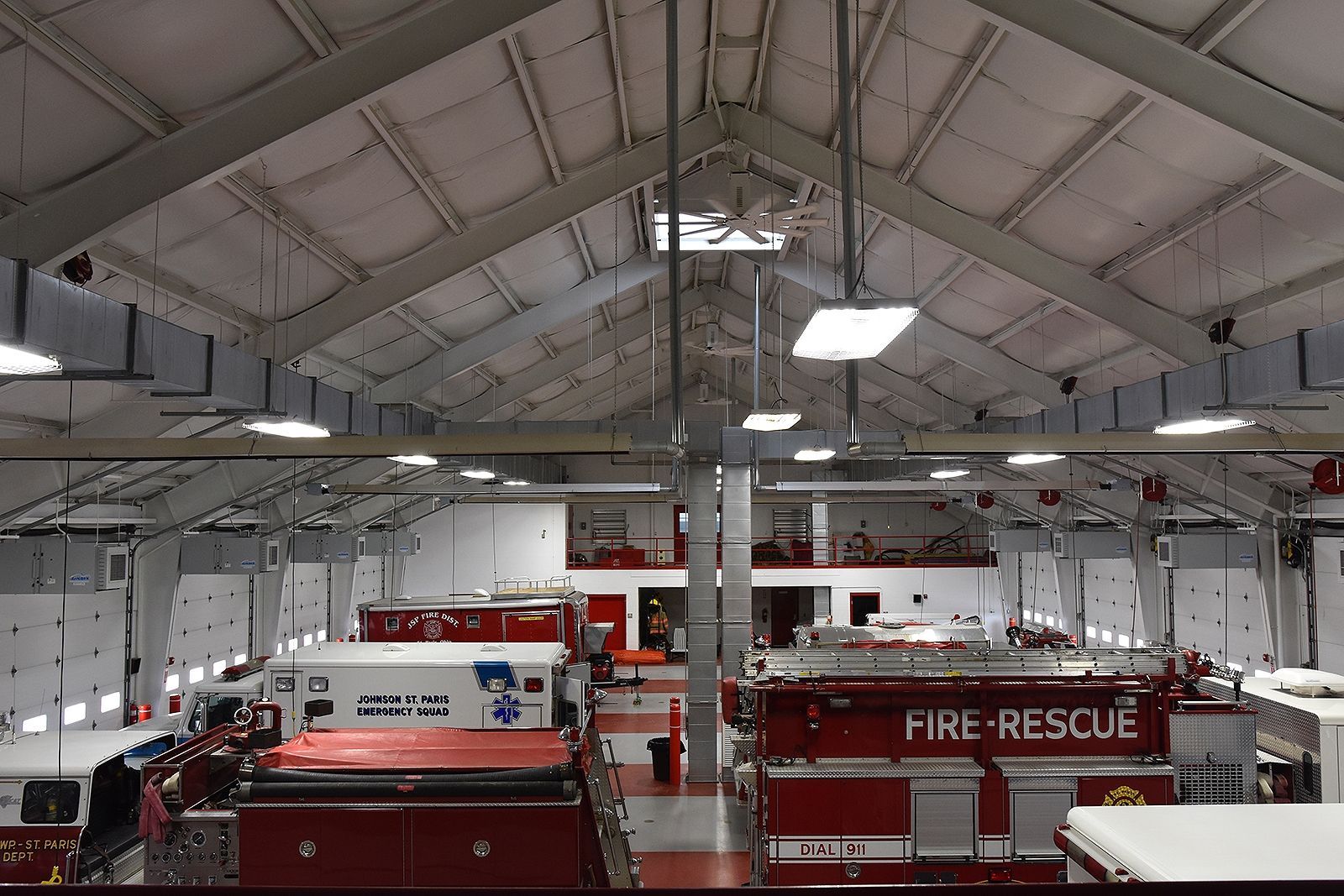 Fire station interior with red fire trucks, ambulance, and high ceiling with overhead lights.