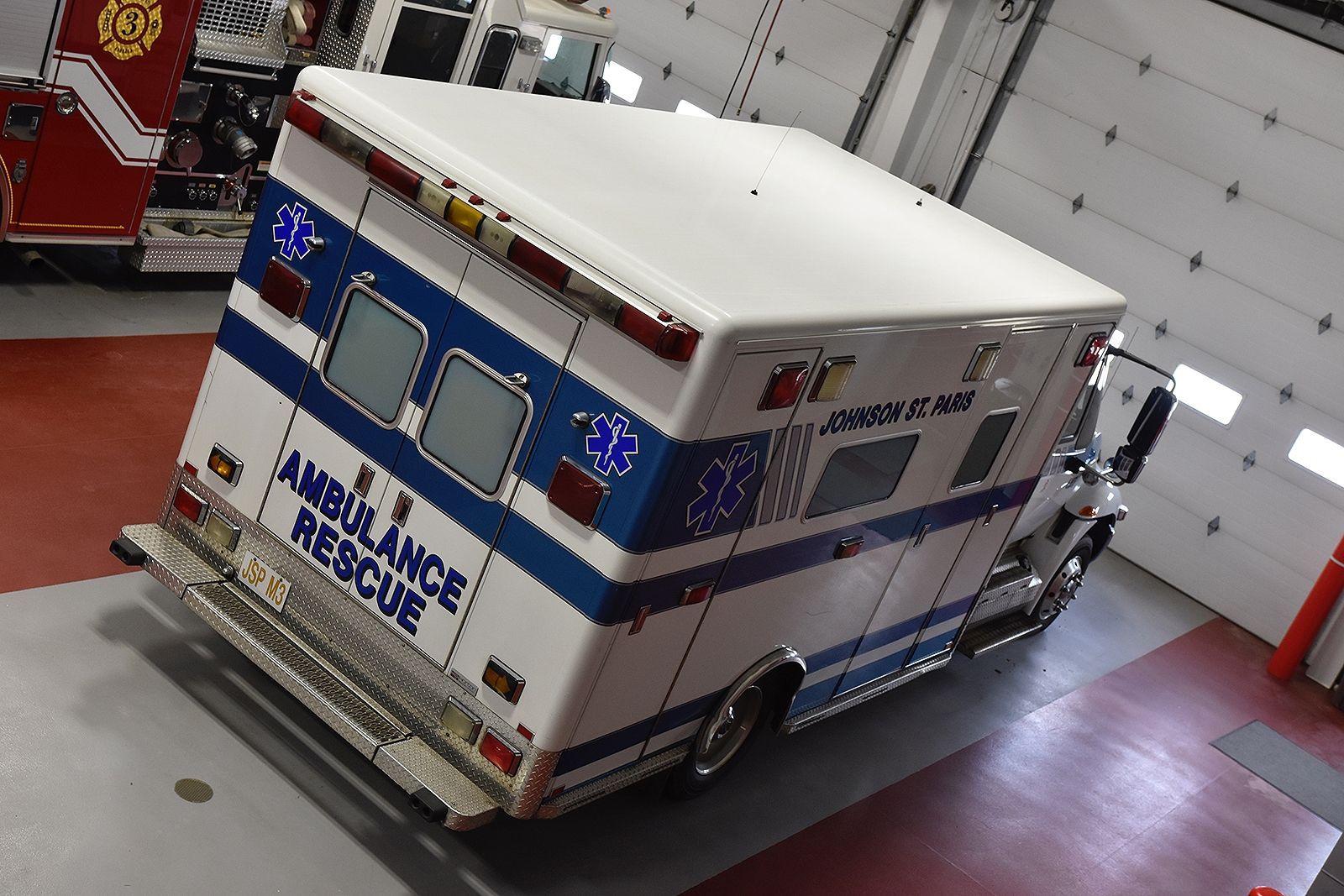 Ambulance rescue vehicle, white and blue, parked inside a garage.