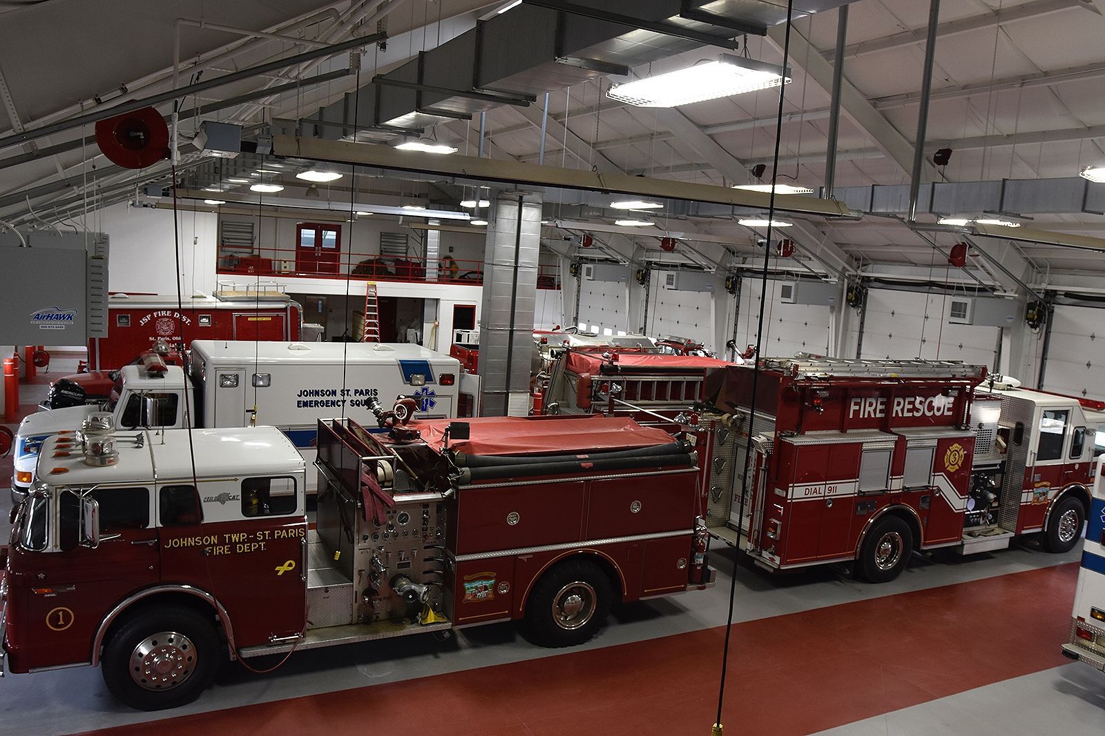 Fire trucks parked inside a fire station bay. Red and white vehicles.