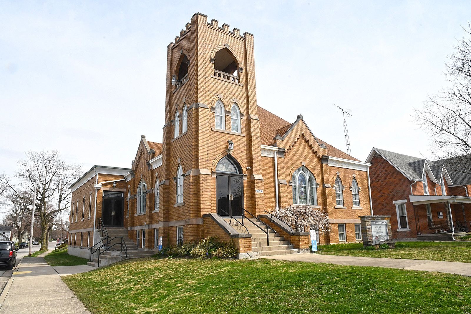 Brick church with a tall tower, arched windows, and a grassy lawn on a sunny day.
