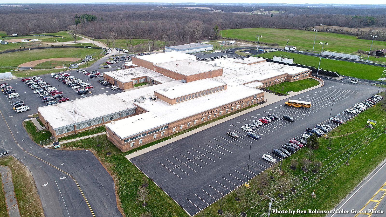 Aerial view of a large, single-story brick building with flat roofs, multiple parking lots, and a school bus.