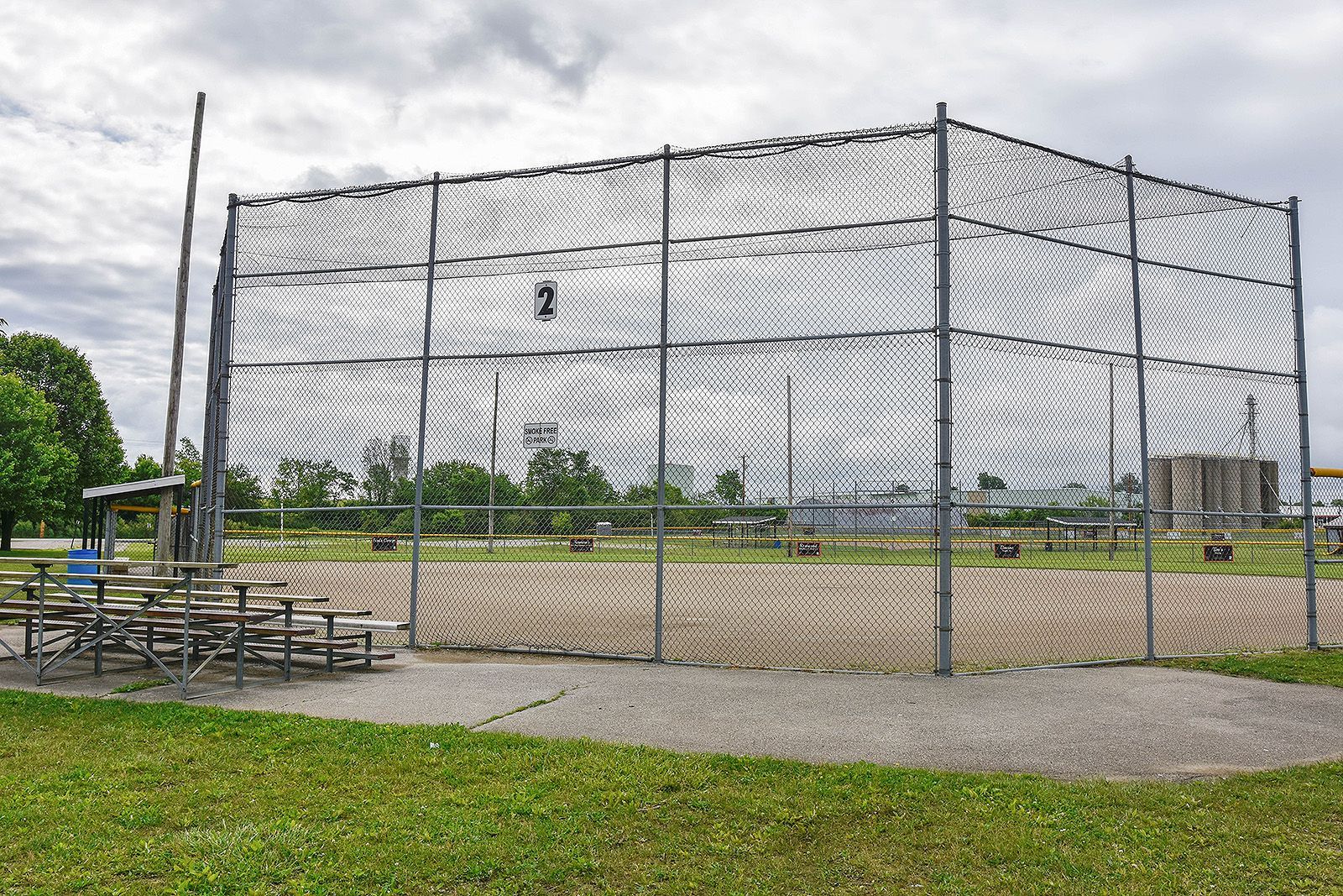 A tall chain-link cage for throwing sports sits on a grassy field, cloudy sky above.