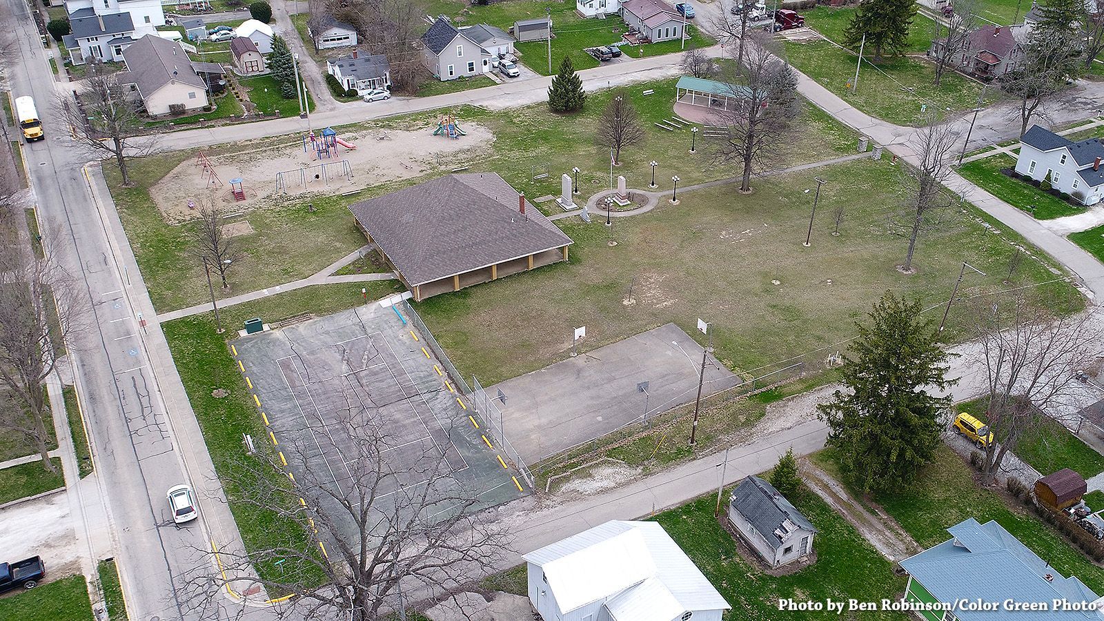 Aerial view of a park with a pavilion, playground, and sports courts in a residential area.