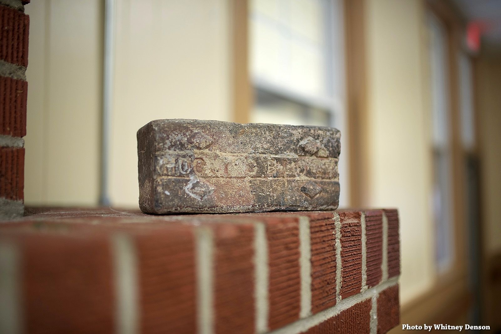 Brick on top of a brick structure, against a blurry window backdrop.
