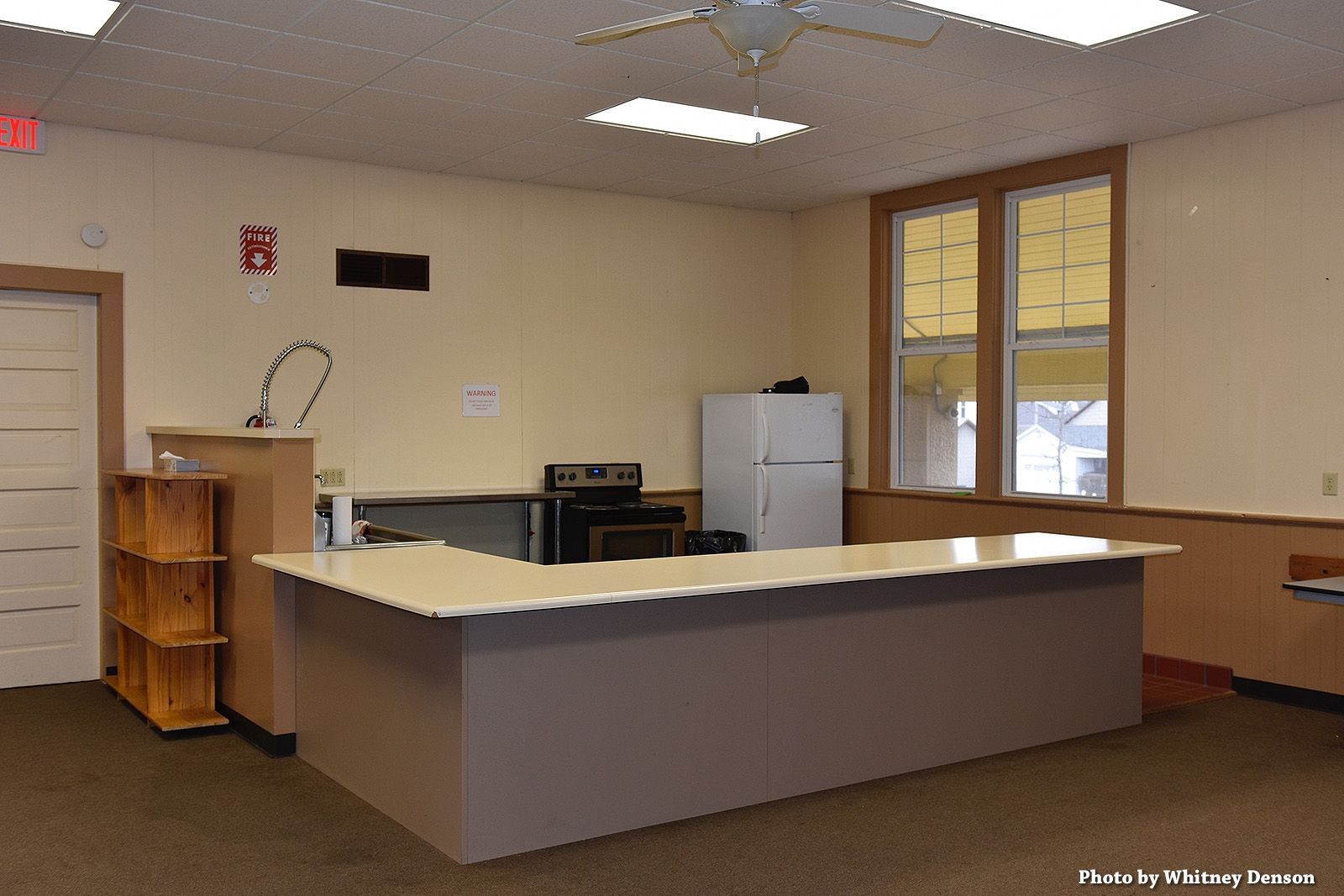 Interior of a room with a counter, refrigerator, oven, and large windows.