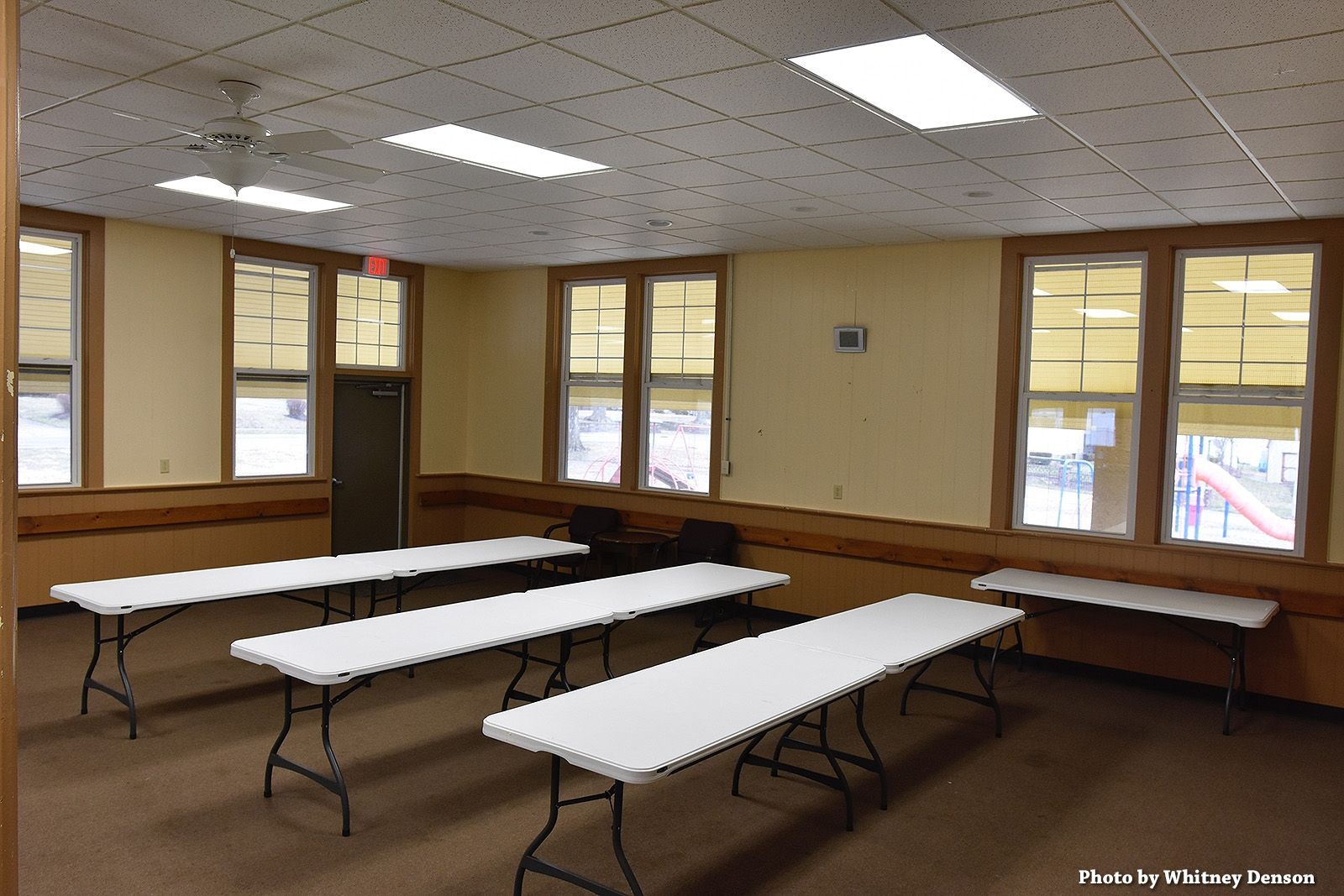 Empty room with folding tables, windows, and ceiling lights.