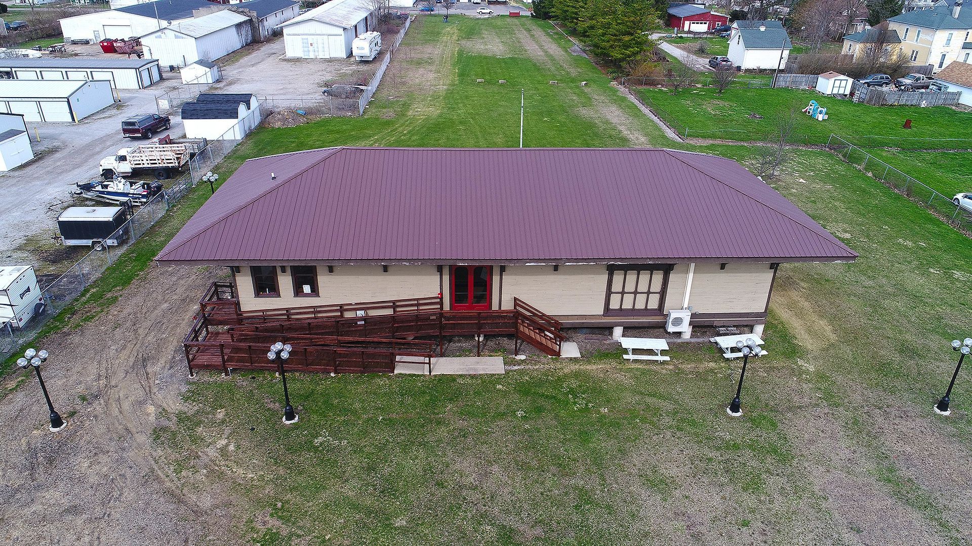 Aerial view of a long, single-story building with a burgundy roof, surrounded by grass and other buildings.