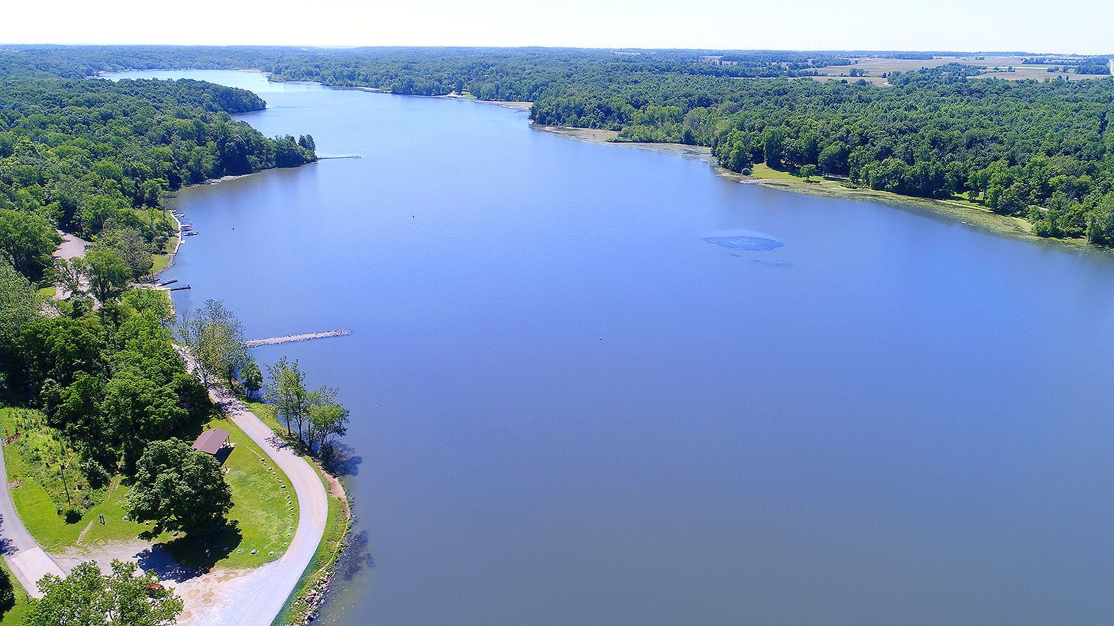 Aerial view of a wide river with forested banks and a walking path on the left.