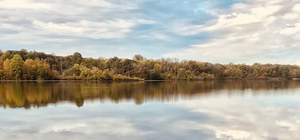 A lake reflecting a forested shoreline and a cloudy sky.