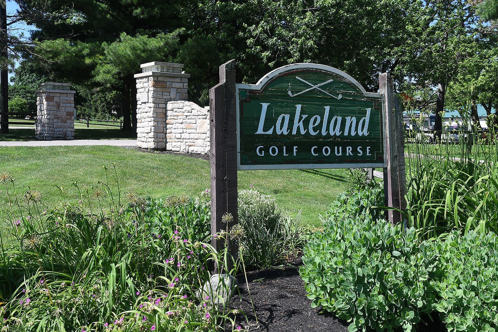 Lakeland Golf Course sign with green background, grassy area, and stone pillars.
