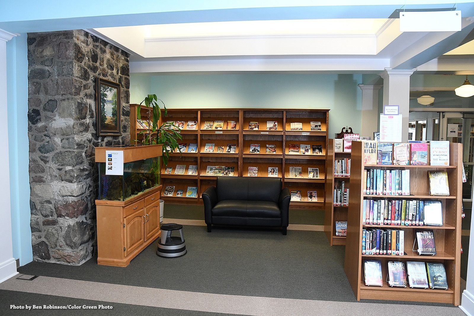 Library interior with bookshelves, a black armchair, and a fish tank by a stone wall.