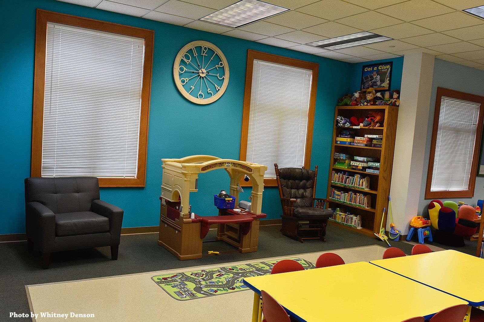 A playroom with teal walls, windows, and toy playhouse.