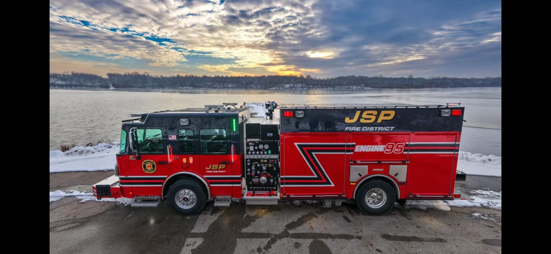 Red fire truck parked next to a body of water under a cloudy sky.