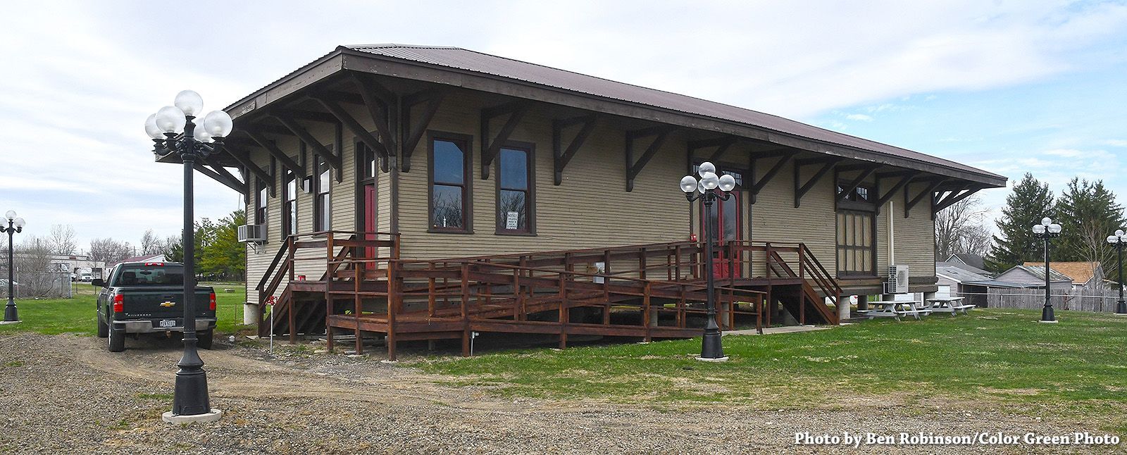A wooden train depot with a brown roof and a pickup truck parked near the building.