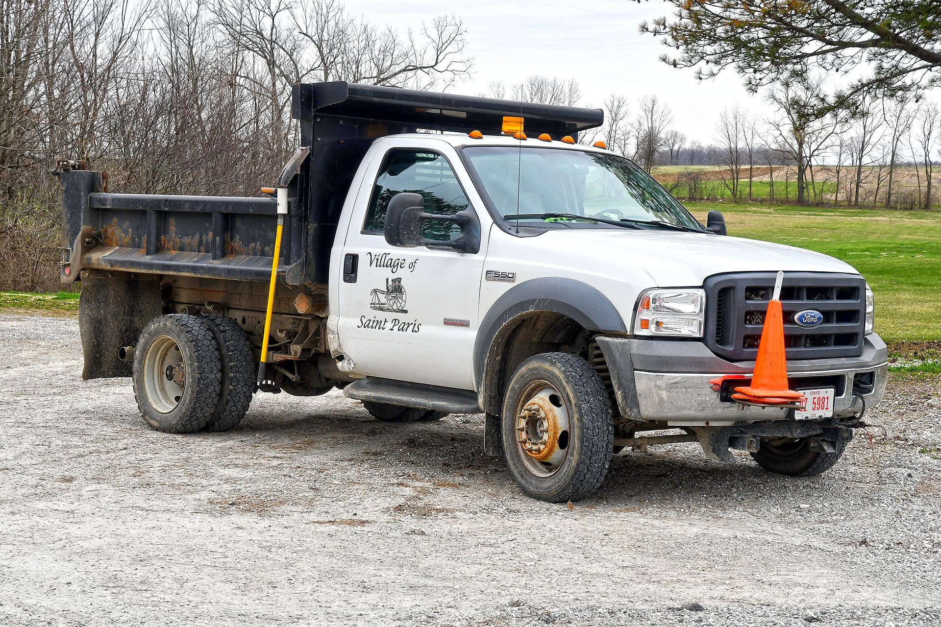 White dump truck parked on gravel. Orange traffic cone attached to the front bumper.