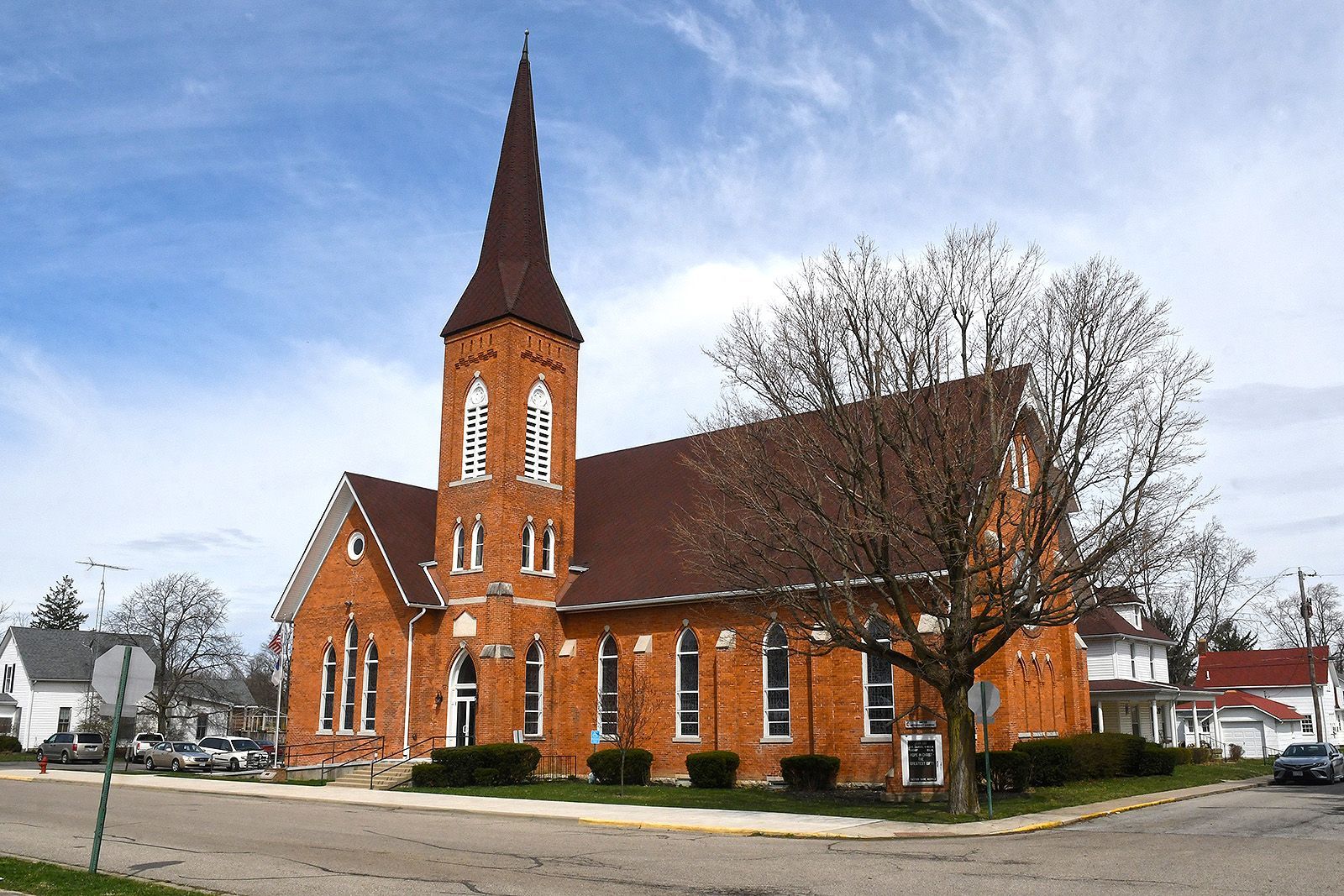 Brick church with steeple, brown roof, and several windows on a sunny day.
