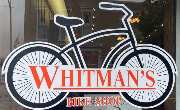 Whitman's Bike Shop logo on glass window with a bicycle outline and orange text.